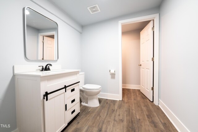 half bathroom with visible vents, baseboards, toilet, wood finished floors, and vanity