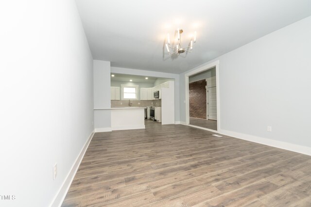 unfurnished living room with a notable chandelier, wood finished floors, and baseboards