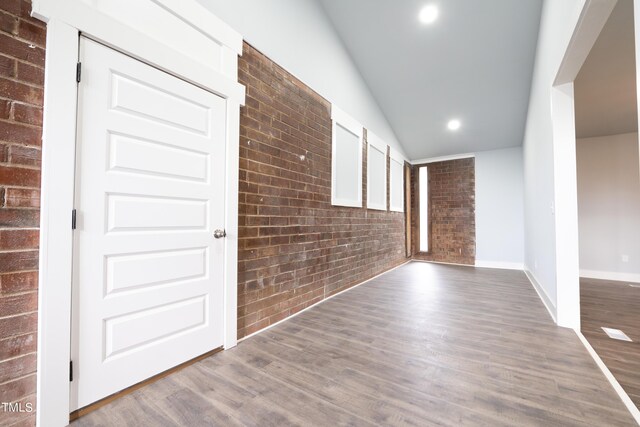 spare room with brick wall, baseboards, lofted ceiling, and wood finished floors