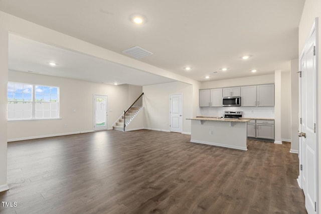 kitchen featuring a center island with sink, gray cabinets, appliances with stainless steel finishes, dark hardwood / wood-style floors, and a kitchen breakfast bar