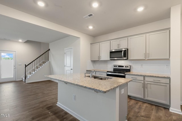 kitchen featuring appliances with stainless steel finishes, gray cabinetry, dark hardwood / wood-style floors, a center island with sink, and sink