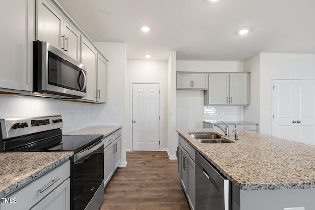 kitchen featuring sink, a kitchen island with sink, dark wood-type flooring, appliances with stainless steel finishes, and decorative backsplash