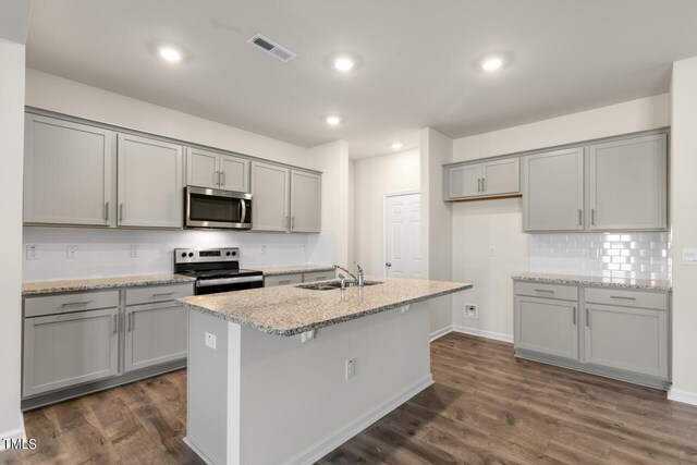 kitchen with stainless steel appliances, light stone counters, dark wood-type flooring, and sink