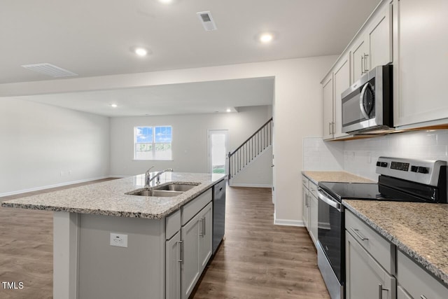 kitchen featuring appliances with stainless steel finishes, backsplash, wood-type flooring, a kitchen island with sink, and sink