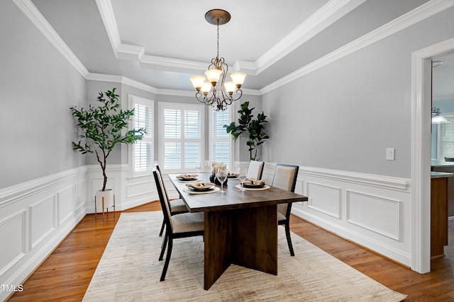 dining room featuring light wood-type flooring, a chandelier, crown molding, and a raised ceiling