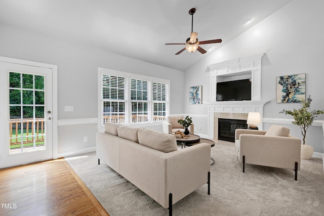 living room featuring ceiling fan, light hardwood / wood-style flooring, a tiled fireplace, and lofted ceiling