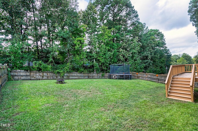 view of yard with a trampoline, a fire pit, and a wooden deck