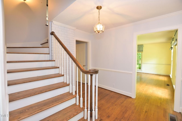 stairway featuring crown molding, wood-type flooring, and an inviting chandelier