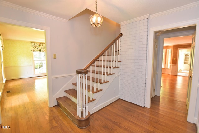 staircase featuring wood-type flooring, an inviting chandelier, and ornamental molding