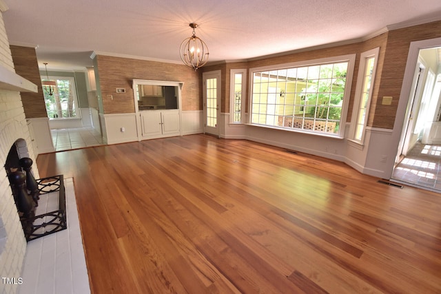 unfurnished living room featuring light wood-type flooring, a fireplace, a notable chandelier, and a healthy amount of sunlight