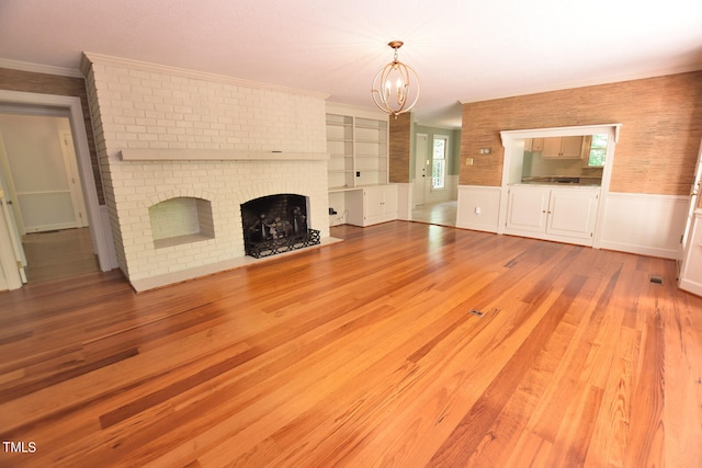 unfurnished living room featuring a fireplace, crown molding, light wood-type flooring, a notable chandelier, and built in features