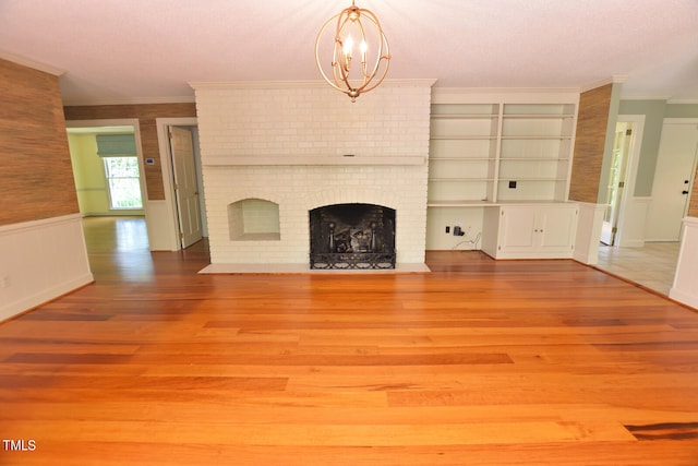 unfurnished living room with hardwood / wood-style floors, a fireplace, a chandelier, and crown molding