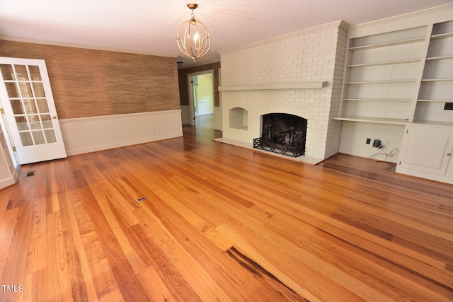 unfurnished living room featuring crown molding, a notable chandelier, a brick fireplace, and hardwood / wood-style flooring