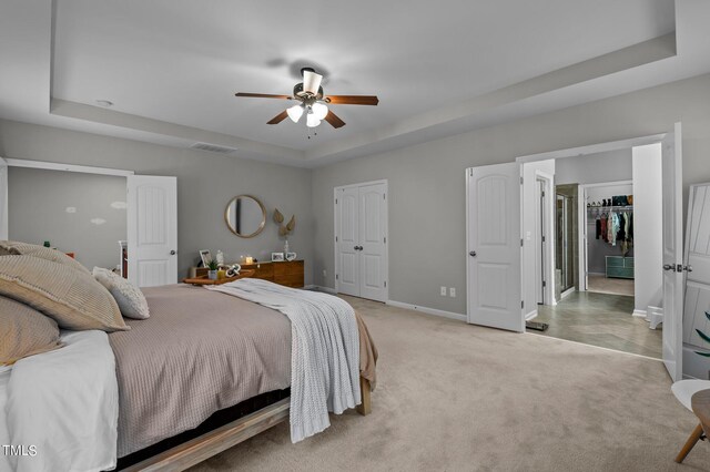 carpeted bedroom with a raised ceiling and ceiling fan