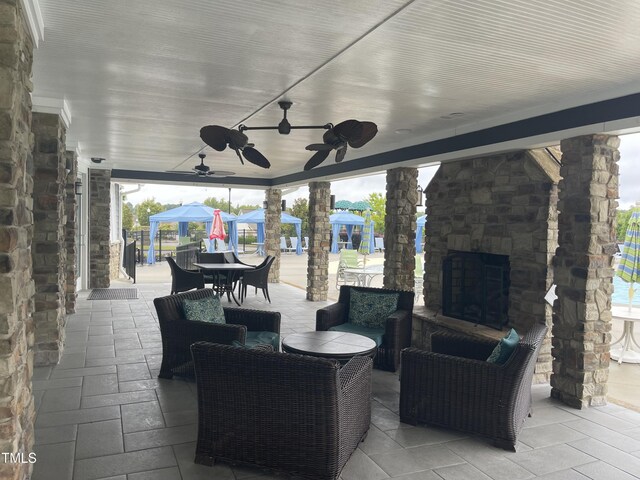 view of patio with an outdoor living space with a fireplace, a gazebo, and ceiling fan