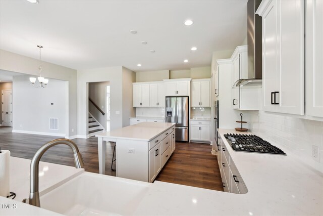 kitchen featuring a kitchen island, white cabinets, appliances with stainless steel finishes, and wall chimney range hood