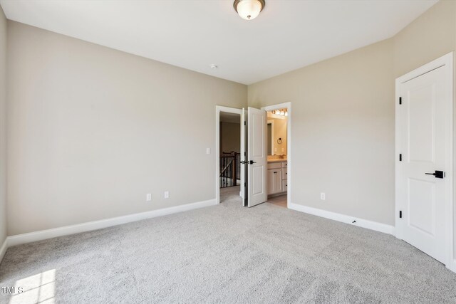 unfurnished bedroom featuring light carpet and ensuite bathroom