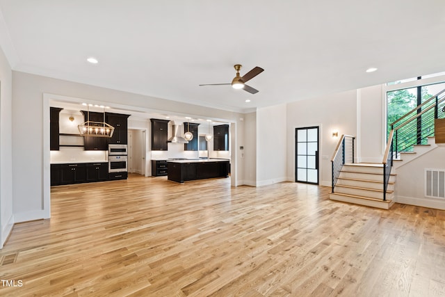 unfurnished living room featuring ceiling fan with notable chandelier, light hardwood / wood-style floors, and ornamental molding