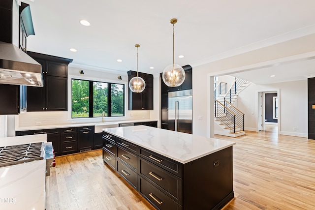 kitchen with stainless steel built in fridge, a kitchen island, light wood-type flooring, decorative light fixtures, and range hood