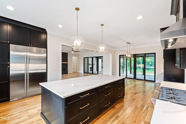 kitchen with built in refrigerator, island exhaust hood, light hardwood / wood-style flooring, decorative light fixtures, and light stone countertops