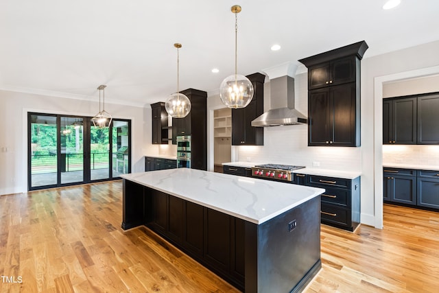 kitchen with wall chimney exhaust hood, pendant lighting, light hardwood / wood-style flooring, and a center island