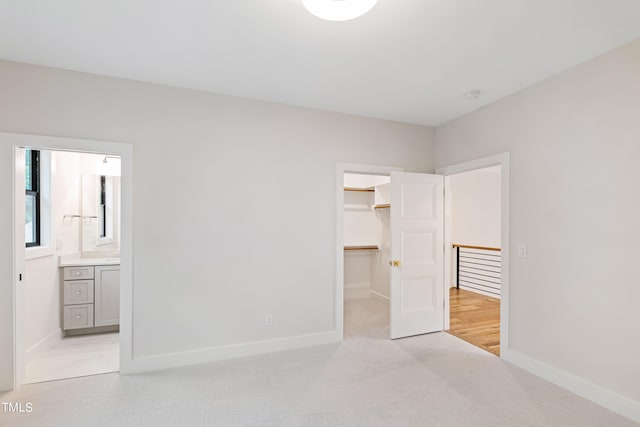 unfurnished bedroom with a closet, a walk in closet, ensuite bathroom, and light carpet