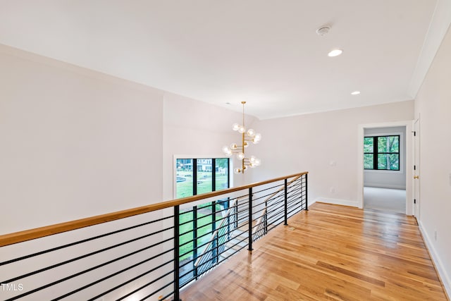 hall featuring ornamental molding, light wood-type flooring, and a notable chandelier