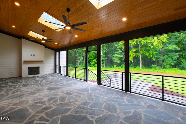 unfurnished sunroom with lofted ceiling with skylight, a wealth of natural light, wooden ceiling, and exterior fireplace