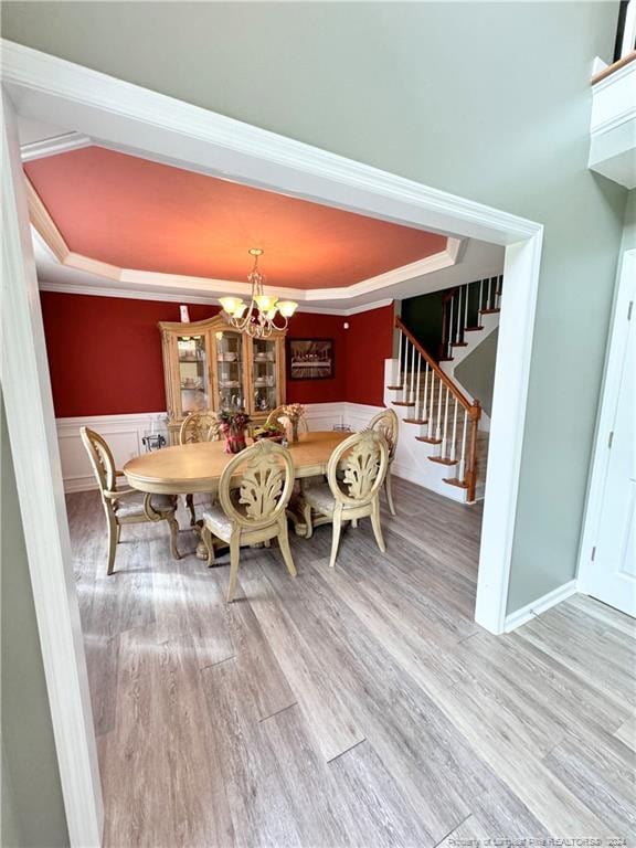 dining room with a raised ceiling, an inviting chandelier, hardwood / wood-style flooring, and crown molding