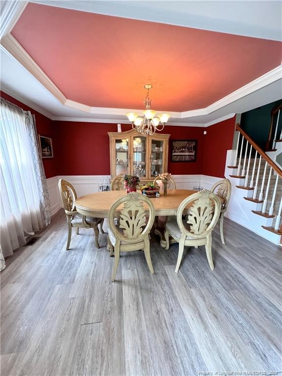 dining space with a tray ceiling, hardwood / wood-style floors, a notable chandelier, and ornamental molding