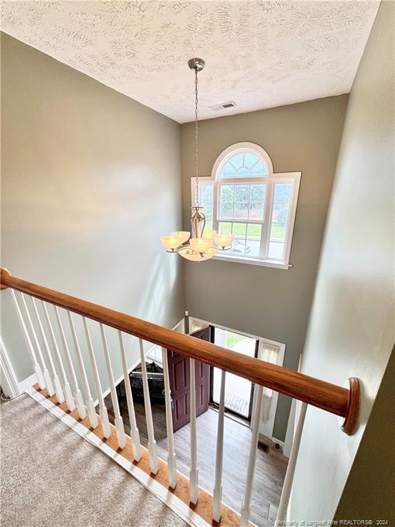 stairway featuring hardwood / wood-style flooring, a chandelier, and a textured ceiling