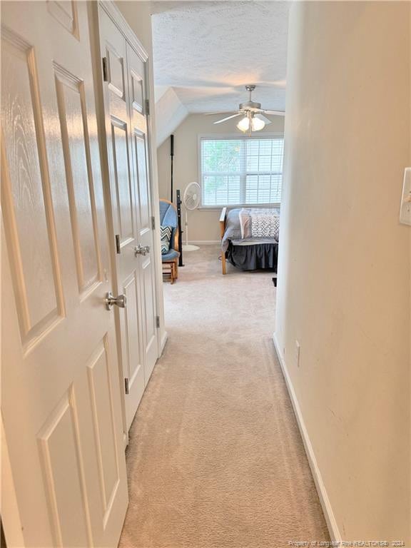 hallway featuring lofted ceiling, a textured ceiling, and light carpet