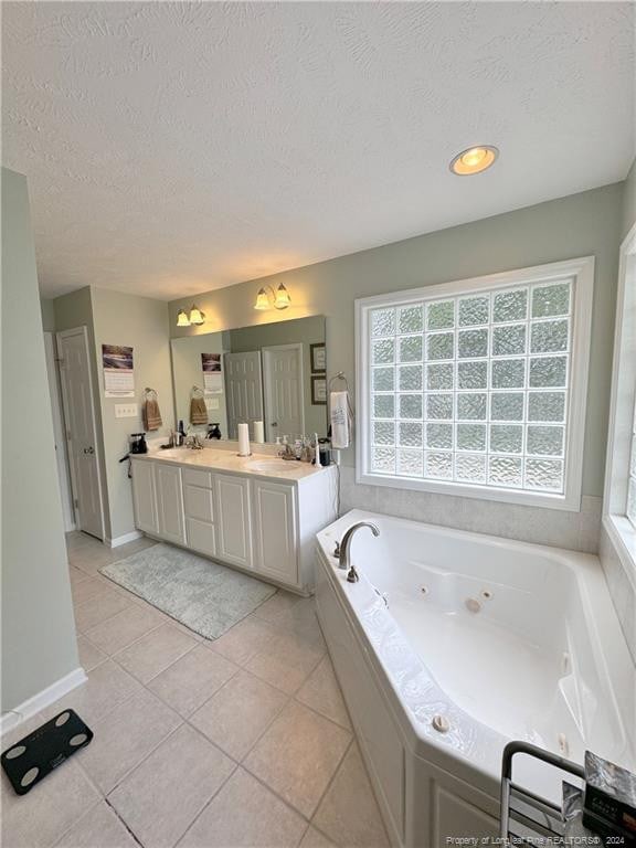 bathroom with a textured ceiling, vanity, a healthy amount of sunlight, and a relaxing tiled tub