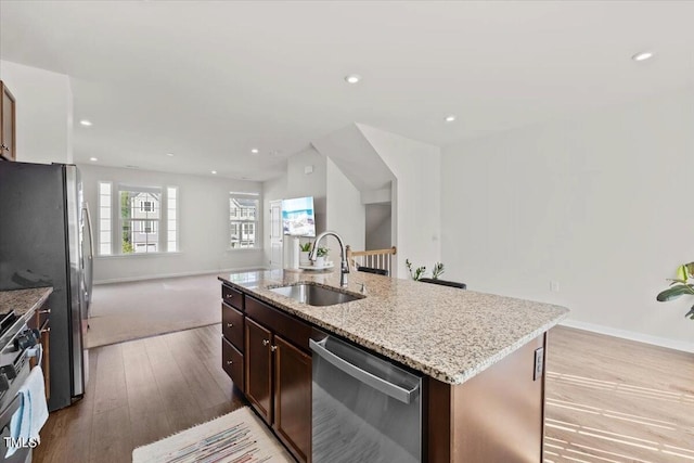 kitchen with light stone countertops, stainless steel appliances, light hardwood / wood-style flooring, a kitchen island with sink, and sink