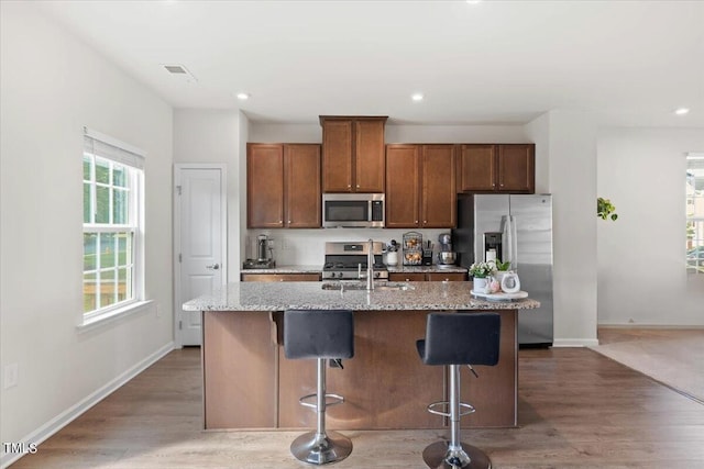 kitchen with an island with sink, stainless steel appliances, a kitchen breakfast bar, and wood-type flooring