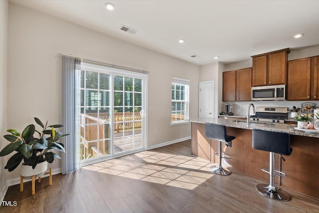 kitchen with light stone counters, light hardwood / wood-style floors, sink, a kitchen bar, and stainless steel appliances