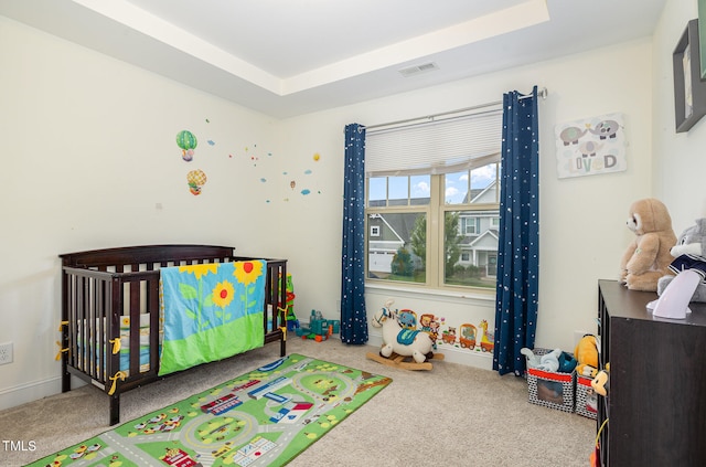 carpeted bedroom with a tray ceiling and a crib