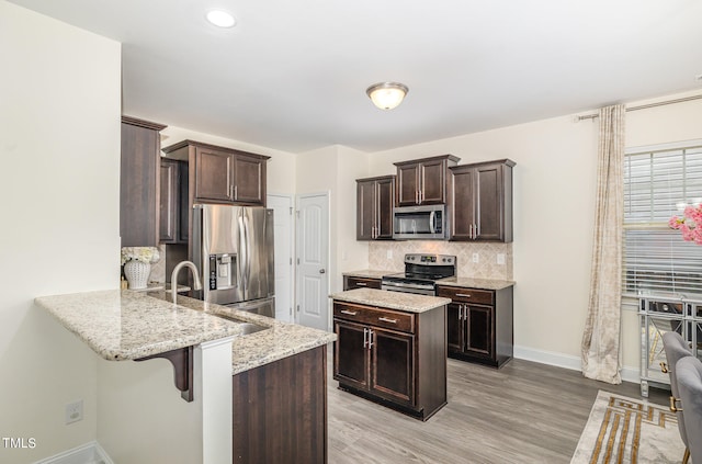 kitchen featuring light wood-type flooring, light stone counters, kitchen peninsula, a kitchen bar, and appliances with stainless steel finishes