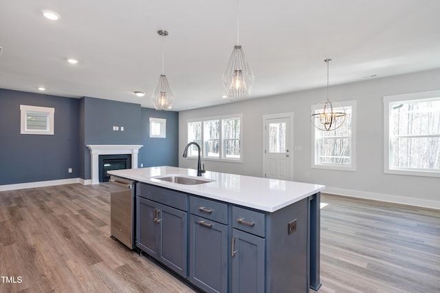 kitchen with sink, hanging light fixtures, light hardwood / wood-style flooring, stainless steel dishwasher, and an island with sink