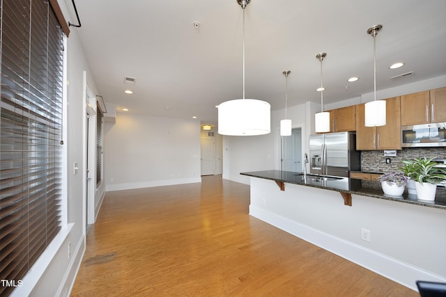 kitchen featuring stainless steel appliances, a kitchen breakfast bar, dark stone counters, decorative light fixtures, and decorative backsplash