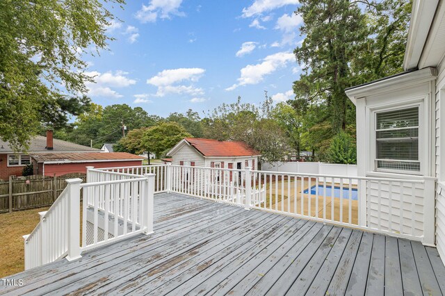 wooden terrace featuring an outdoor structure and a fenced in pool