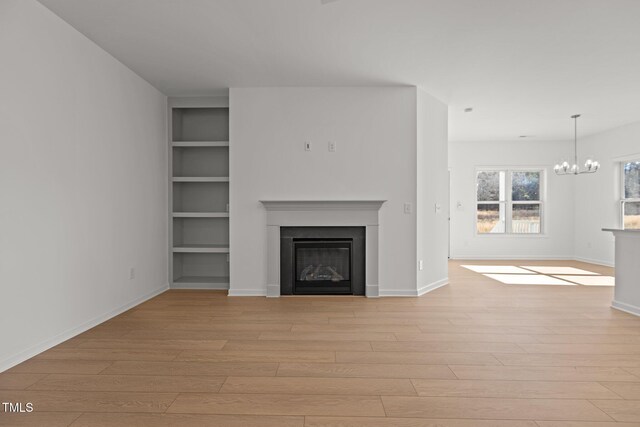 unfurnished living room featuring light hardwood / wood-style floors, built in features, and an inviting chandelier