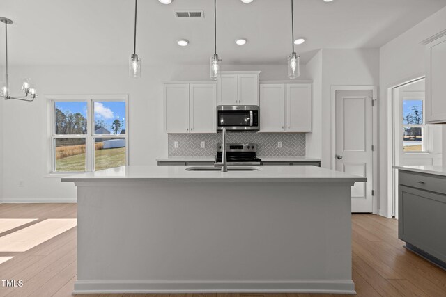 kitchen with stainless steel appliances, hanging light fixtures, and a kitchen island with sink