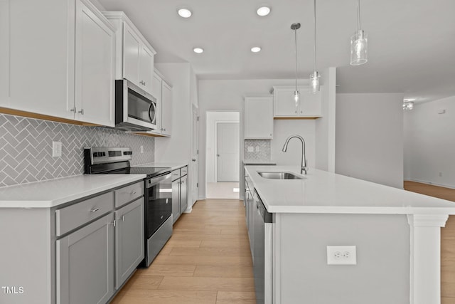 kitchen featuring appliances with stainless steel finishes, an island with sink, hanging light fixtures, and sink