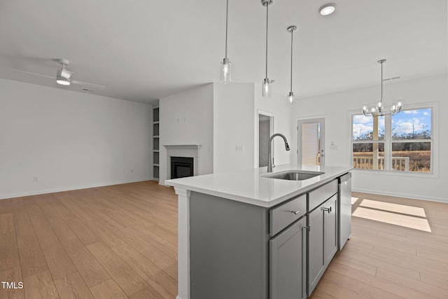 kitchen with gray cabinets, stainless steel dishwasher, sink, a kitchen island with sink, and ceiling fan with notable chandelier