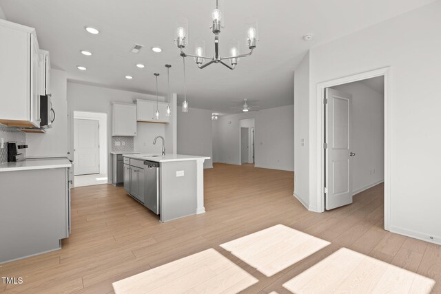 kitchen with decorative light fixtures, backsplash, an island with sink, and ceiling fan with notable chandelier