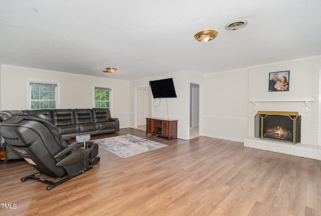 living room with a textured ceiling, crown molding, light hardwood / wood-style flooring, and a brick fireplace