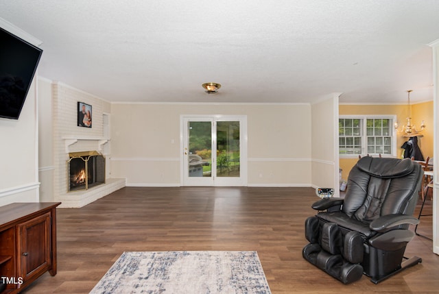 living room with a fireplace, a textured ceiling, ornamental molding, hardwood / wood-style floors, and a notable chandelier