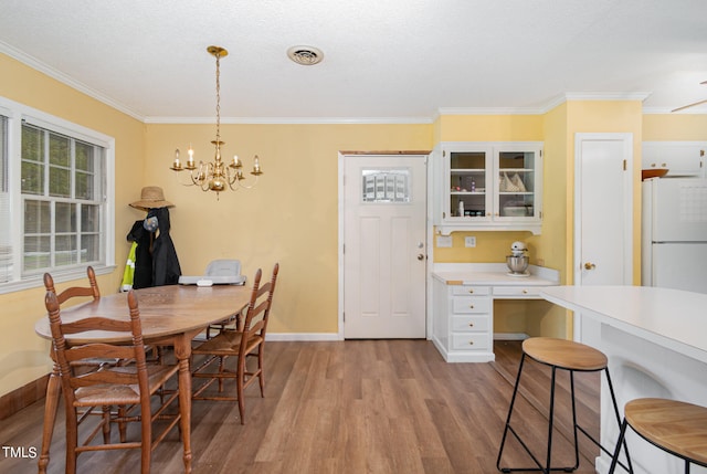 dining room featuring ornamental molding, light wood-type flooring, a chandelier, and a textured ceiling