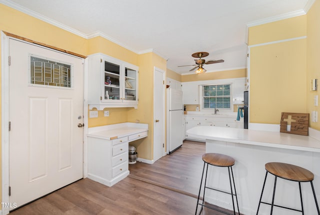 kitchen featuring light hardwood / wood-style floors, white cabinets, white fridge, a kitchen bar, and ceiling fan